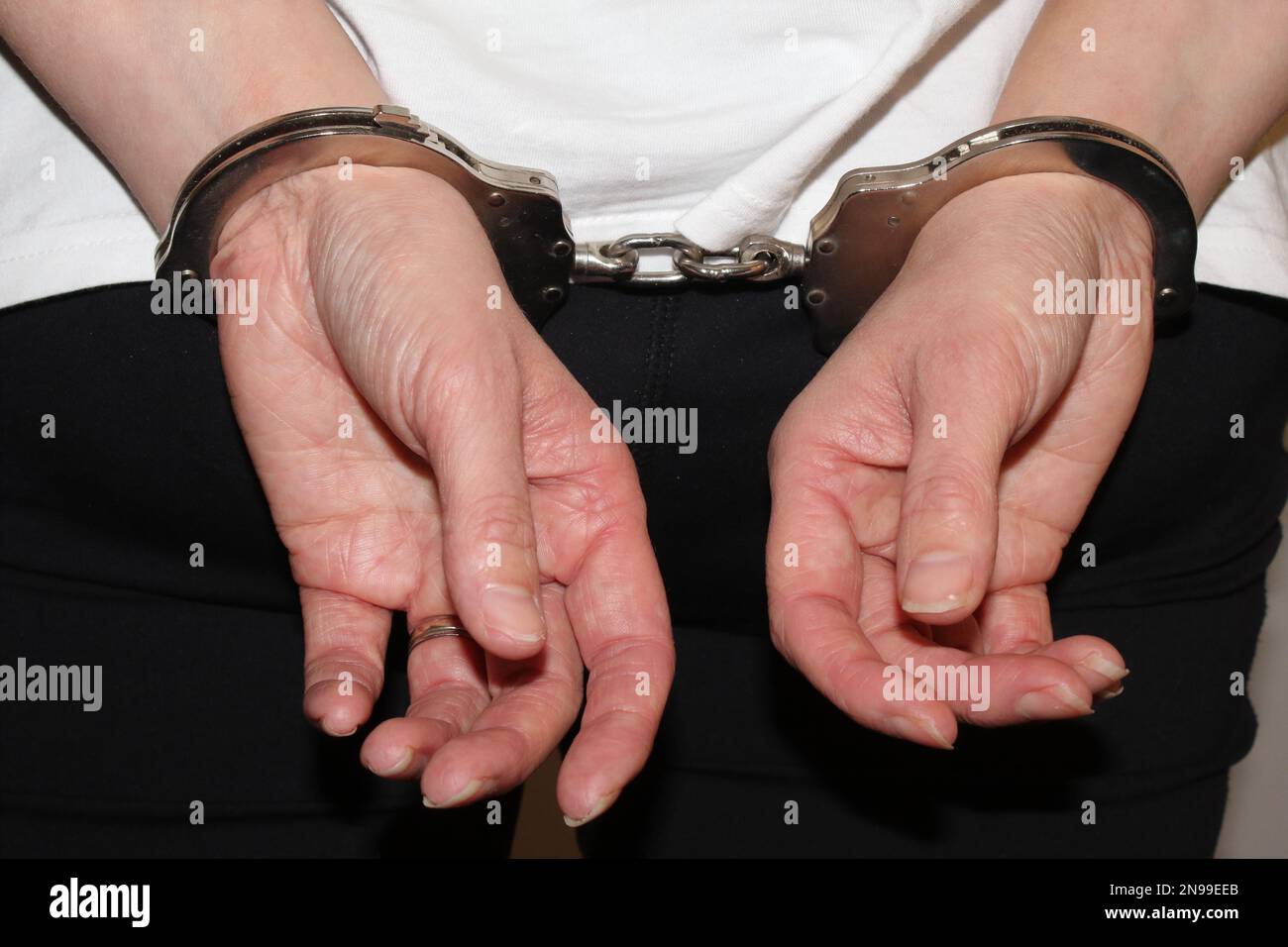 An arrested woman stands with her hands in handcuffs. The prisoner is handcuffed behind her back as she awaits her trip to jail by the police. Stock Photo