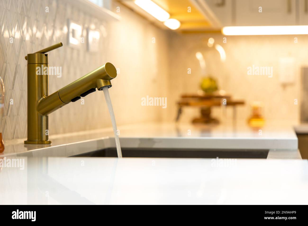 A closeup of a modern golden faucet of a kitchen sink with a blurry background Stock Photo