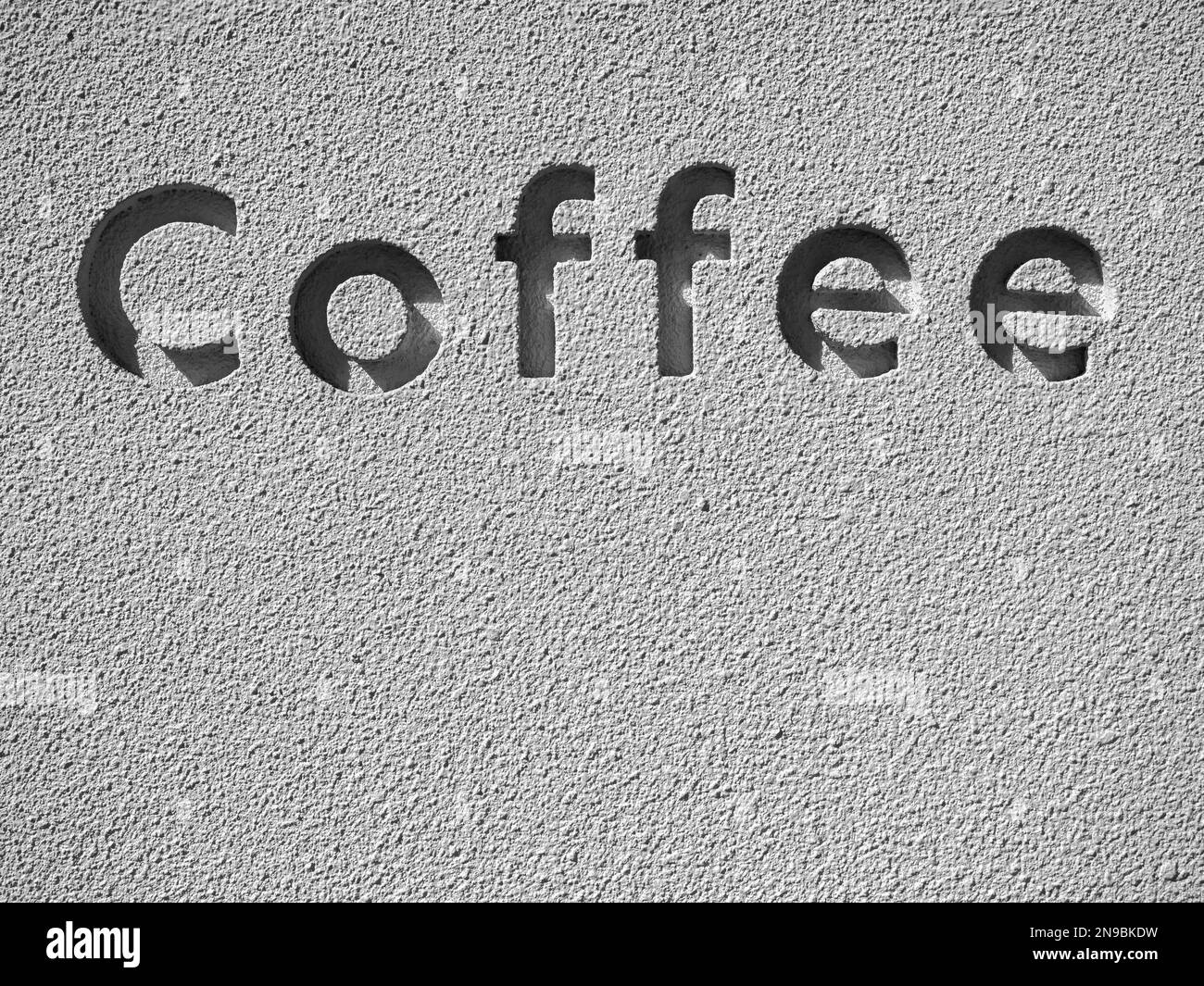 The word "Coffee", the letters carved into the words on the grunge concrete wall with copy space, vertical. Light and shadow in the carving font on th Stock Photo