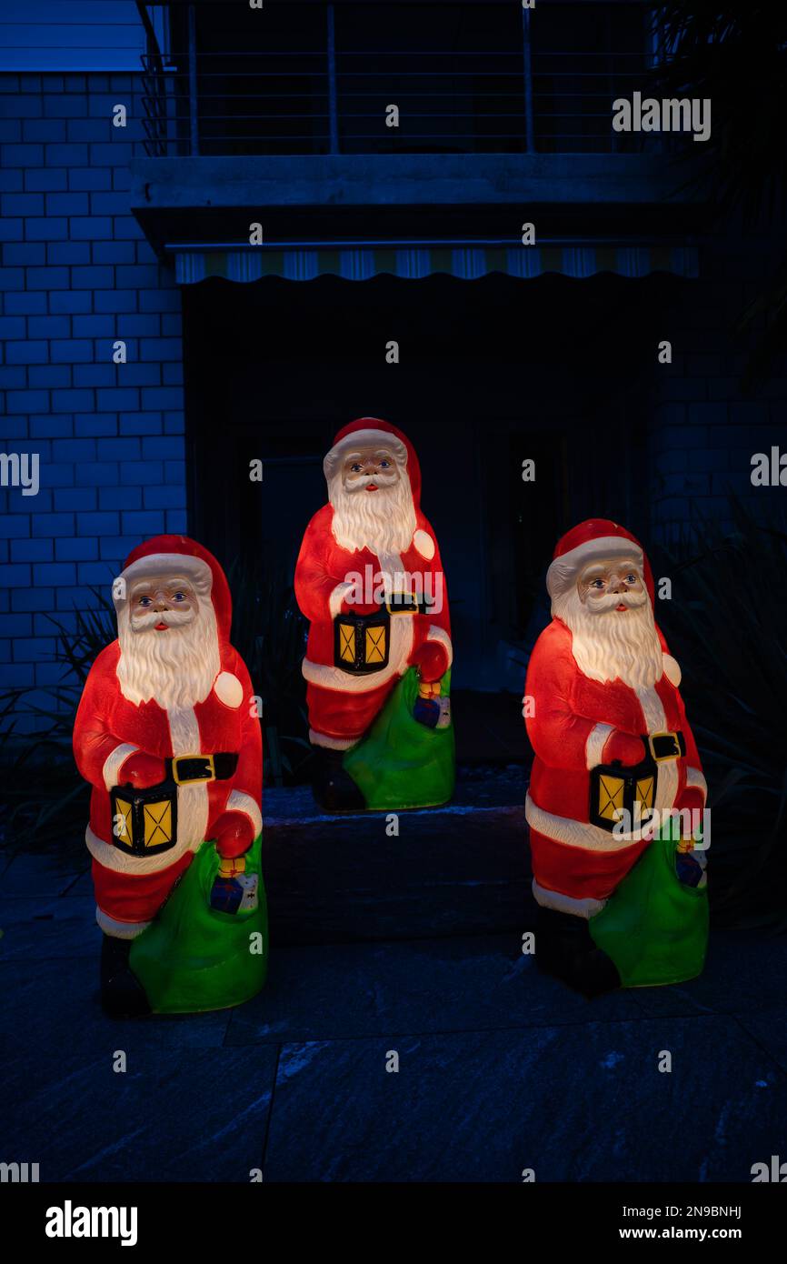 Figures of three Santa Claus at night with lamps in the yard of the house Stock Photo