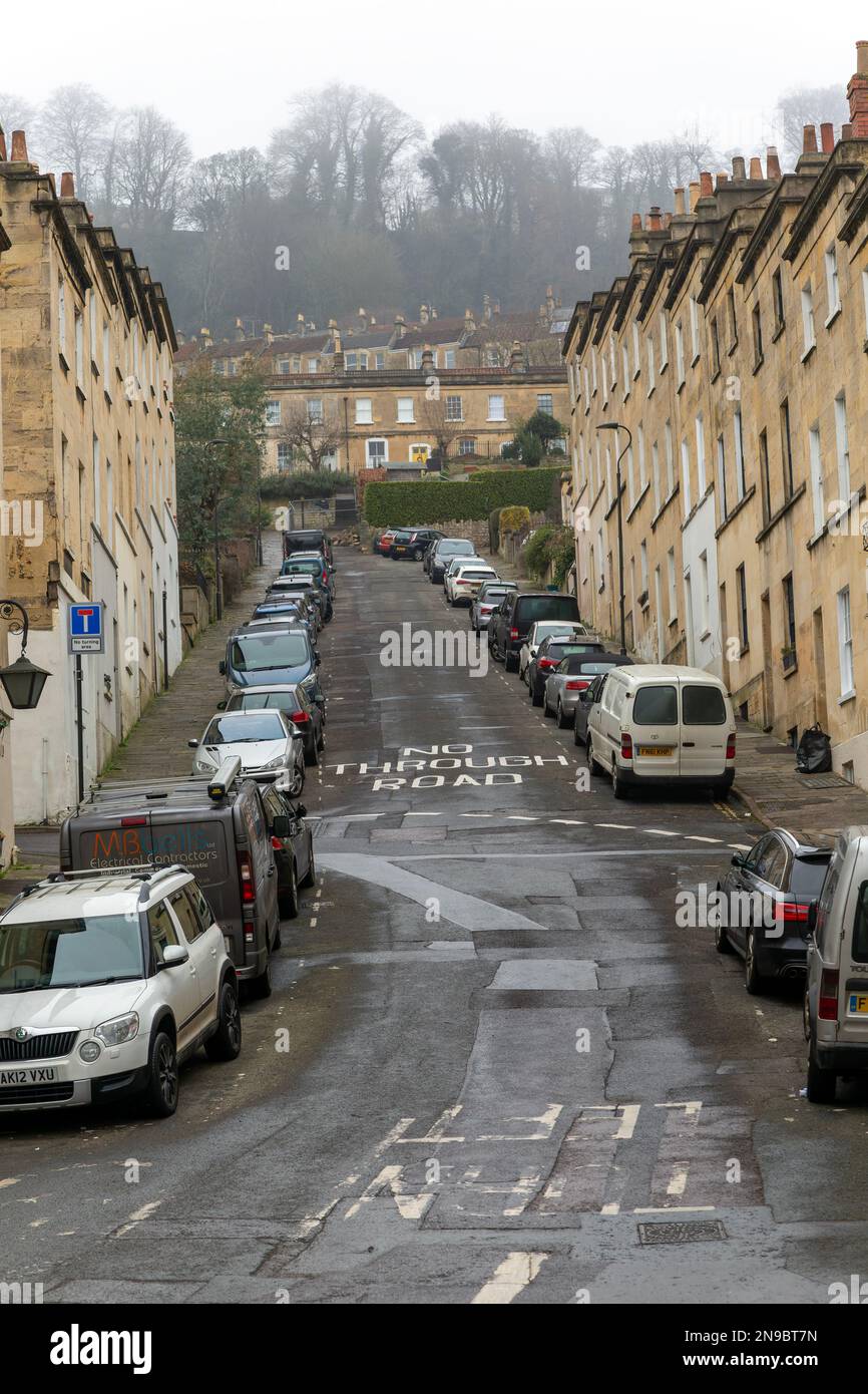 No Through Road sign written on steep road with cars parked on street
