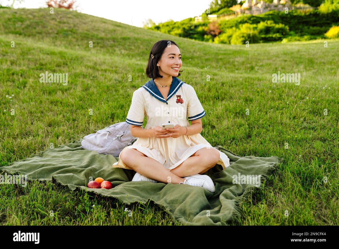 Young cheerful asian girl wearing dress using mobile phone while ...
