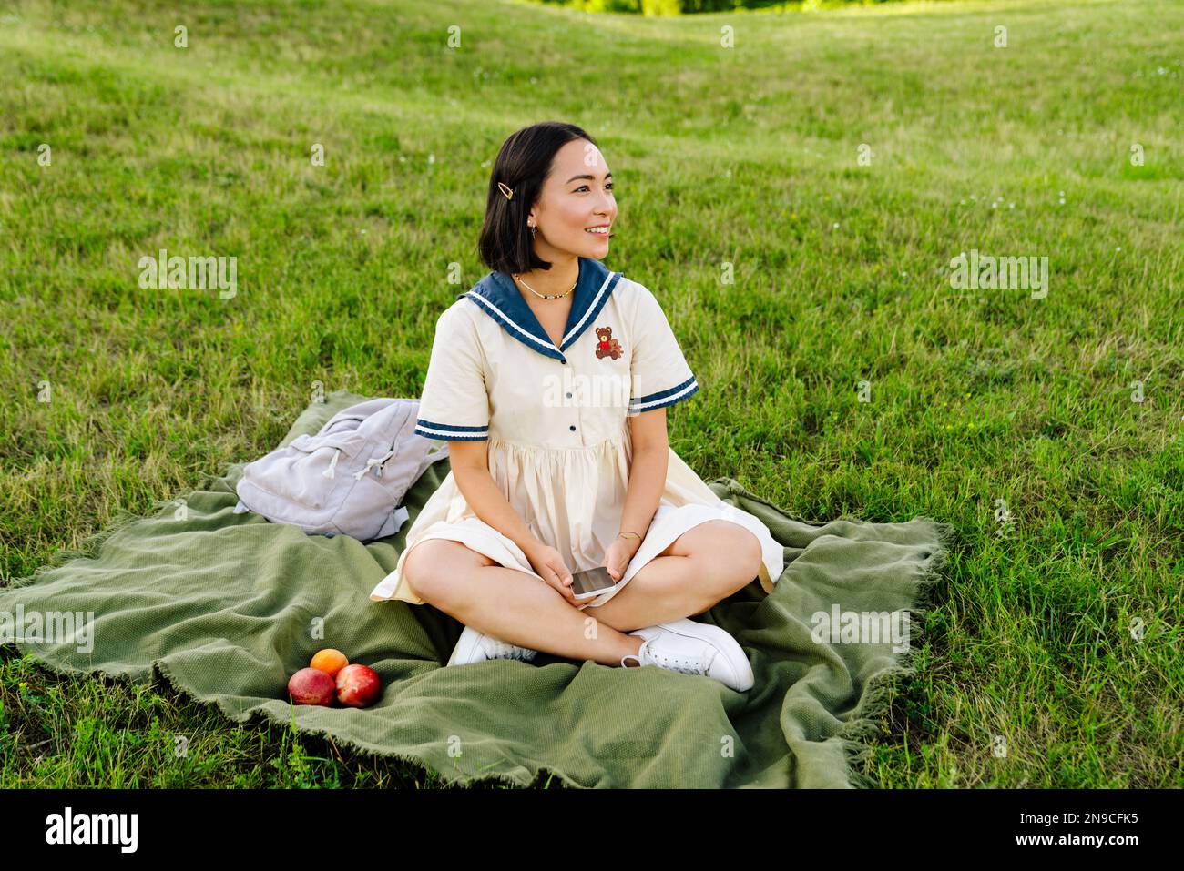 Young cheerful asian girl wearing dress using mobile phone while ...