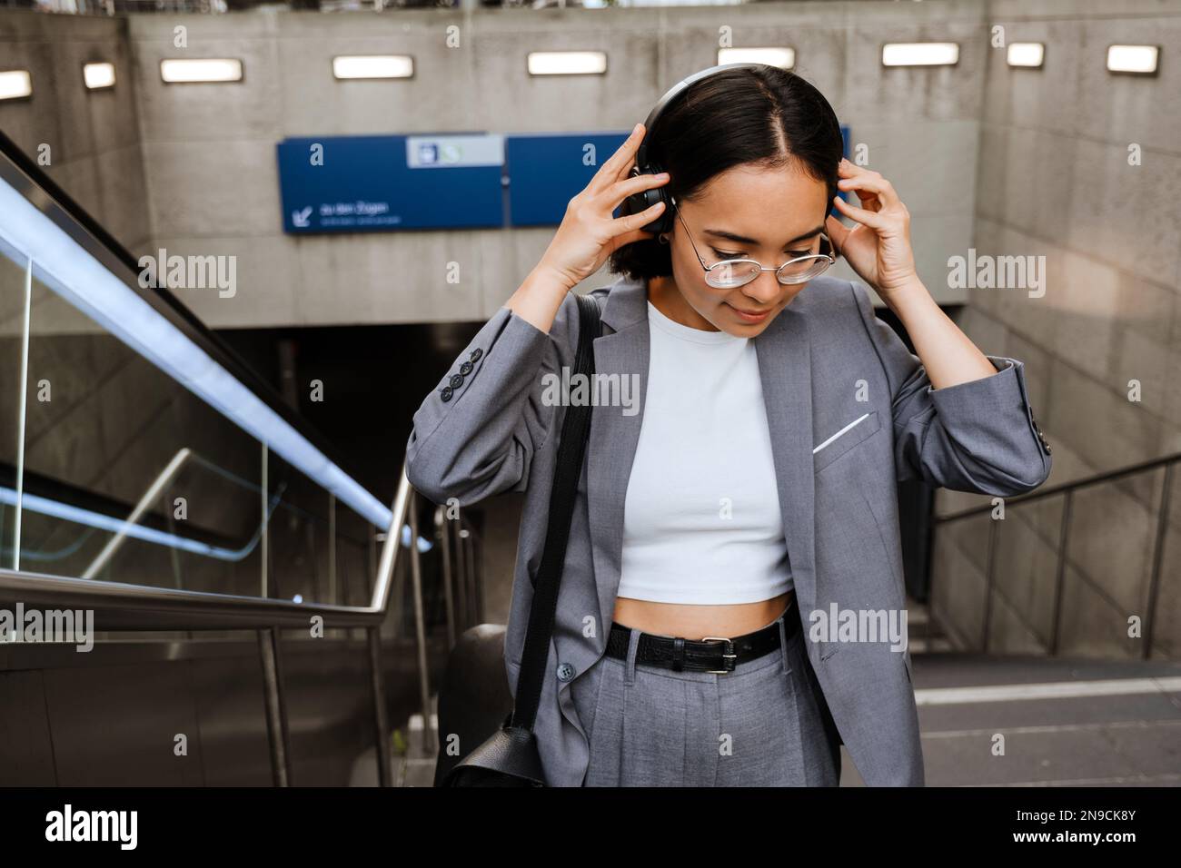 Young asian woman wearing suit putting on headphones while going up stairs outdoors Stock Photo