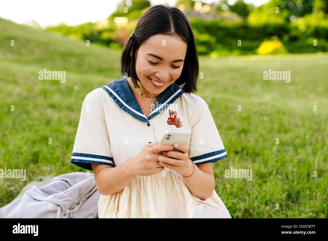 Young cheerful asian girl wearing dress using smartphone while sitting ...