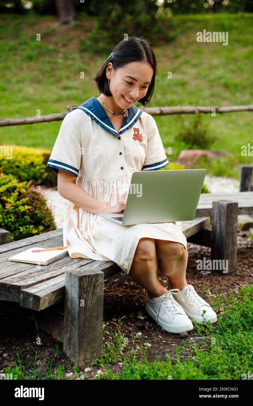Young cheerful asian girl wearing dress using laptop while sitting on ...