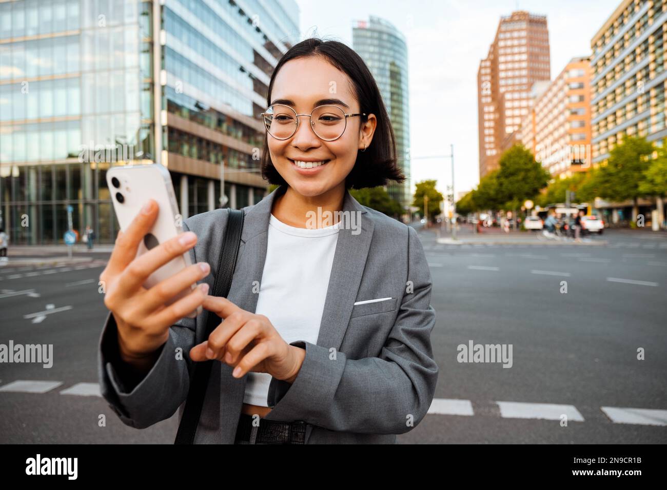 Yound asian woman using cellphone and smiling while standing outdoors at the city street Stock Photo
