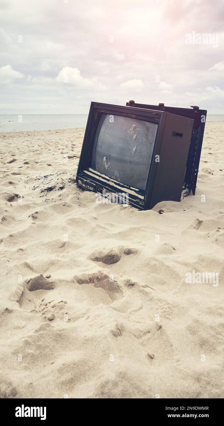 Old broken TV set abandoned on a beach, color toning applied, selective focus. Stock Photo