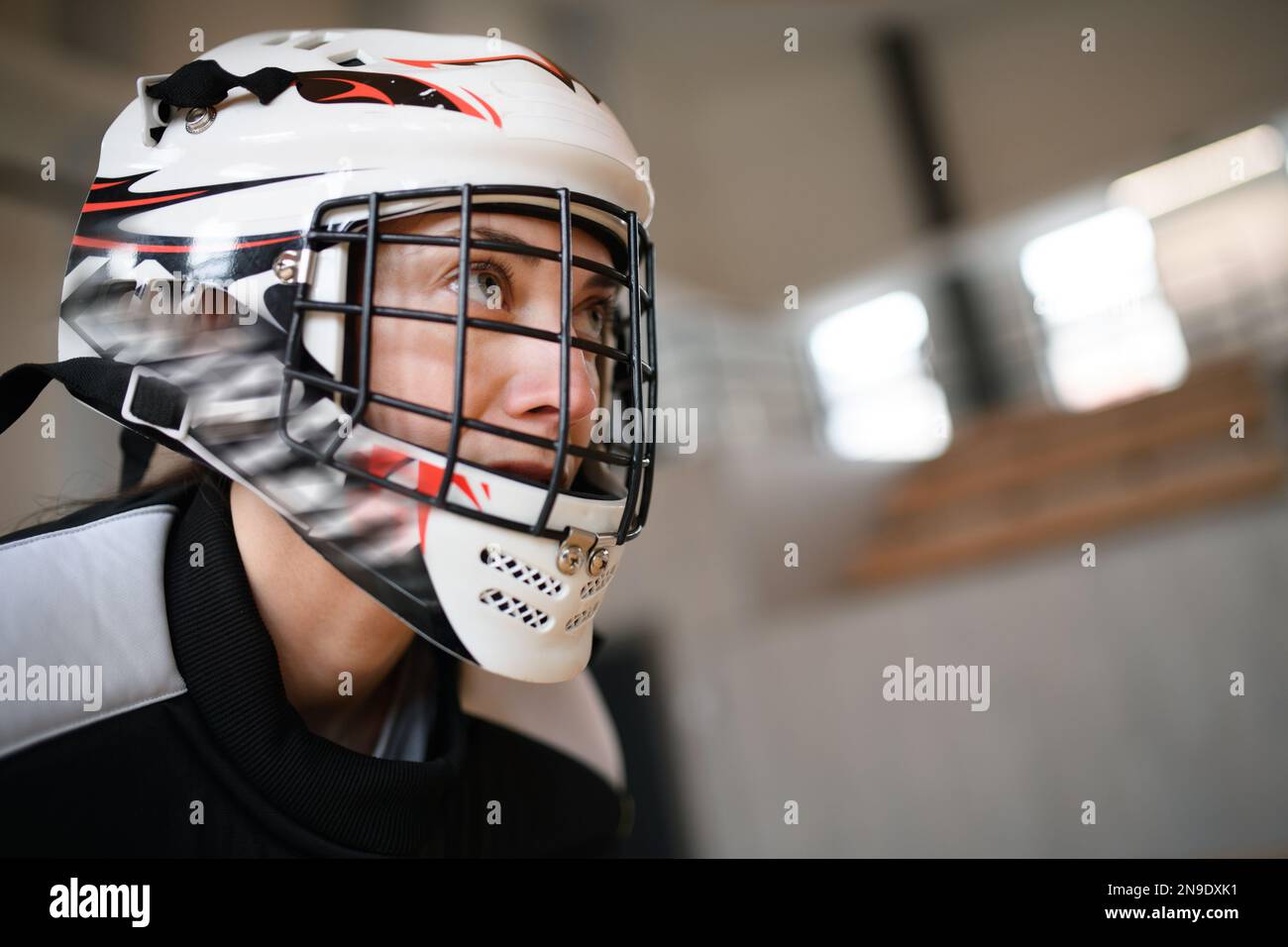 Close-up of woman floorball goalkeeper in helmet concetrating on game in gym. Stock Photo