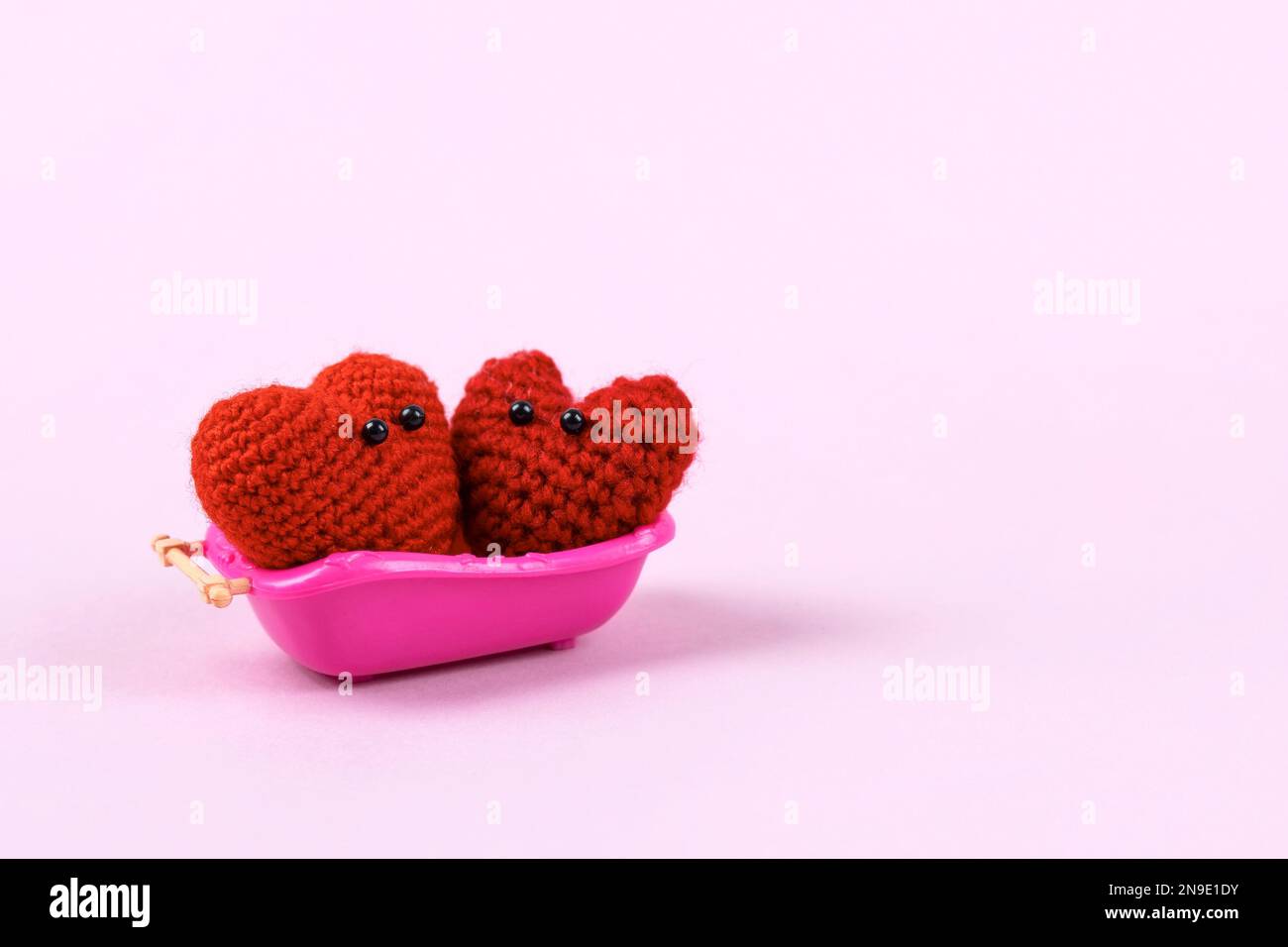 Two knitted hearts with cute faces are washing in a pink bathroom. Love