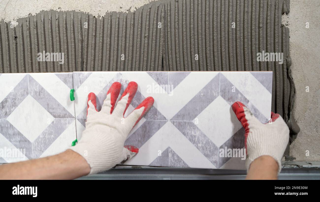 Instaling ceramic tiles. Male hands glue ceramic tiles on the wall in