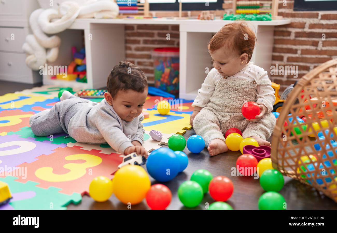Two adorable babies playing with balls sitting on floor at kindergarten ...