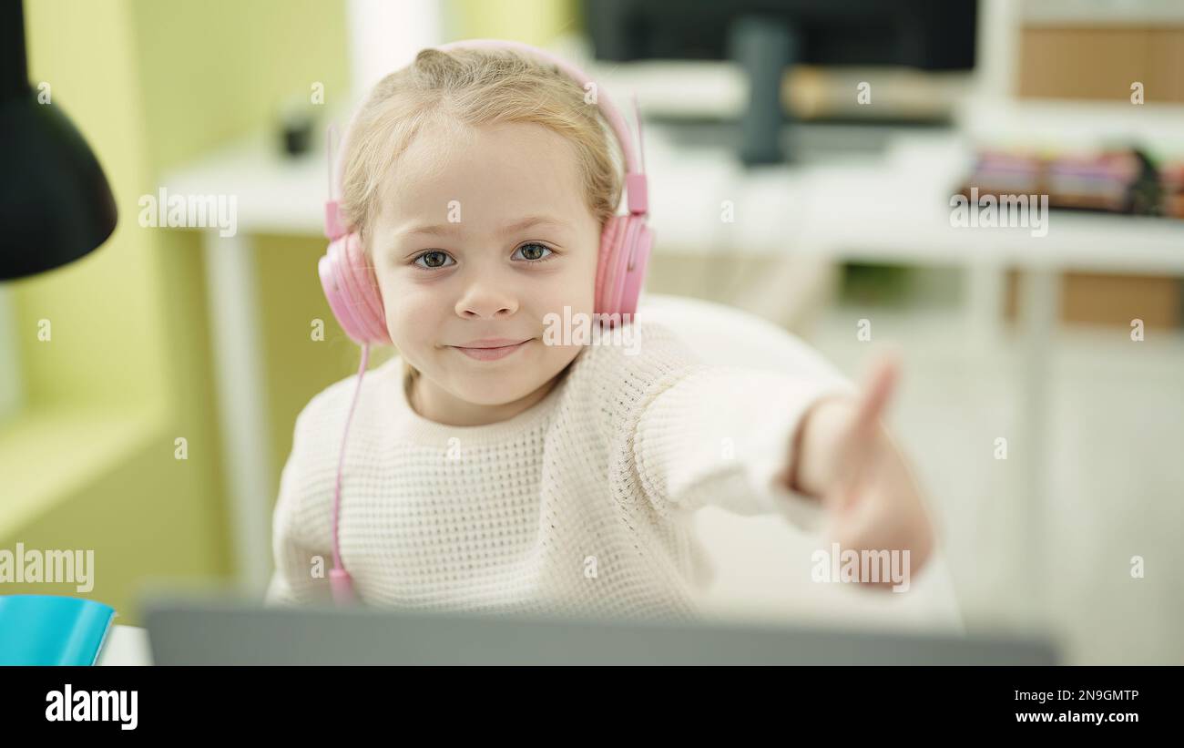 Adorable blonde girl student using laptop and headphones doing ok ...