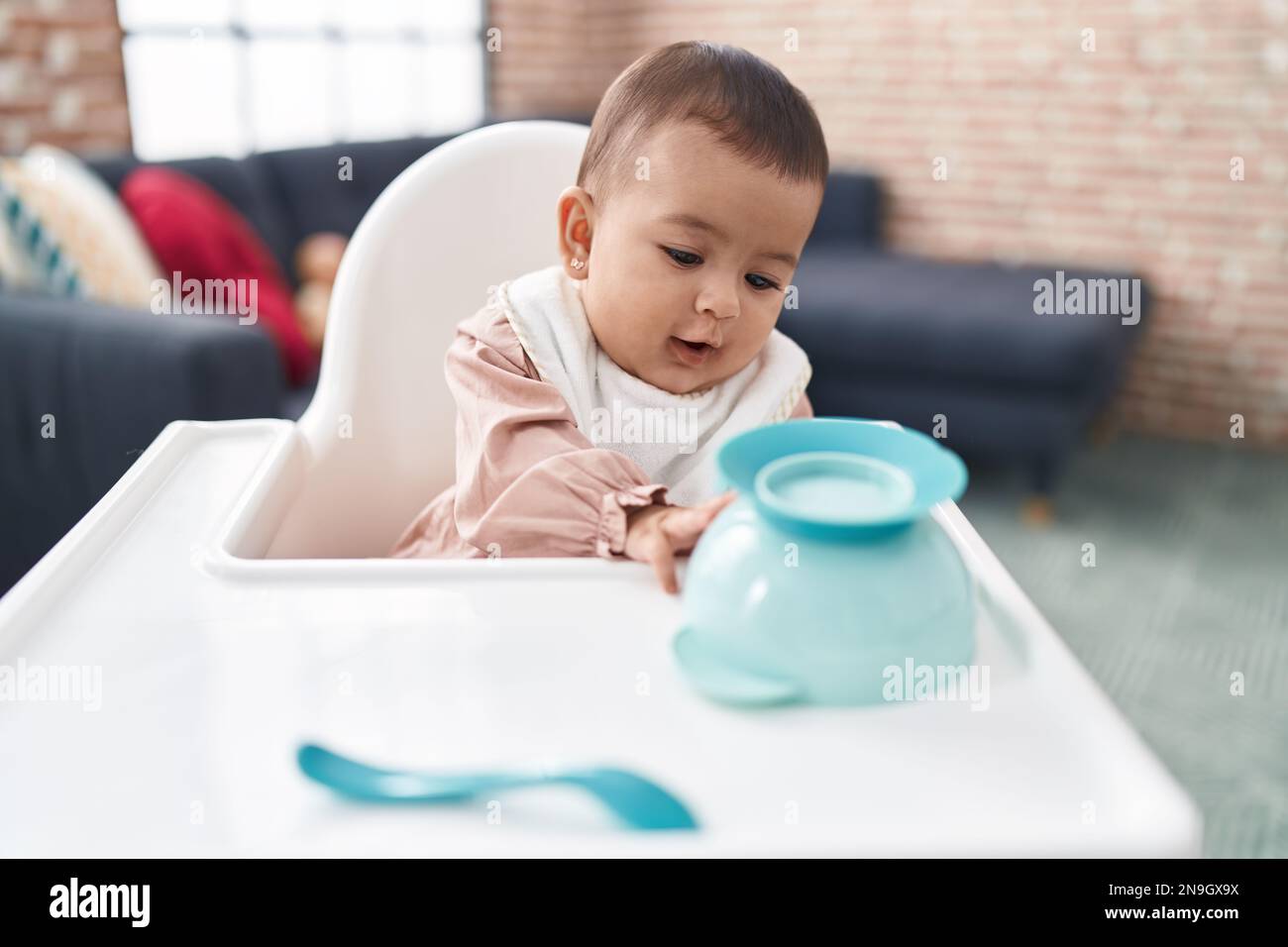 Adorable hispanic baby wearing bib sitting on highchair at home Stock Photo