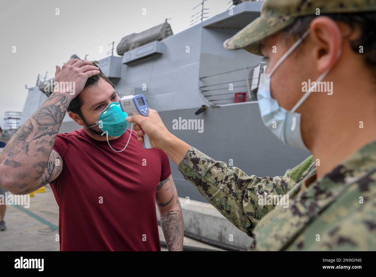 A Sailor assigned to the guided-missile destroyer USS Kidd (DDG 100) has his temperature checked as he returns to the ship as part of the Navy’s aggressive response to the COVID-19 outbreak. Stock Photo