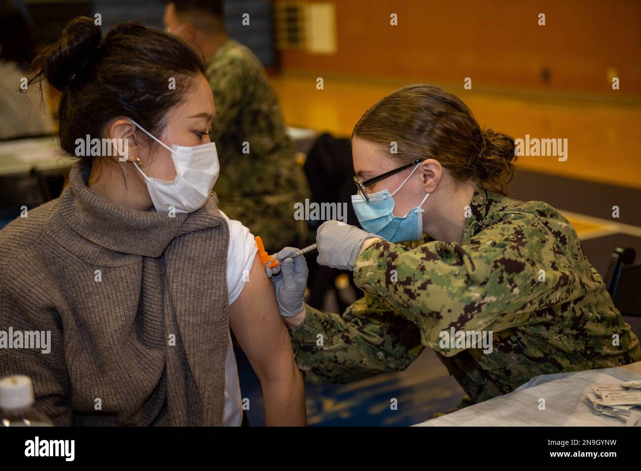 Hospital Corpsman 3rd Class Courtney Minchew, from Ocala, Fla., assigned to the U.S. Navy’s forward-deployed aircraft carrier USS Ronald Reagan (CVN 76), administers a COVID-19 vaccination booster to a Japanese base employee at Commander, Fleet Activities Yokosuka. Stock Photo