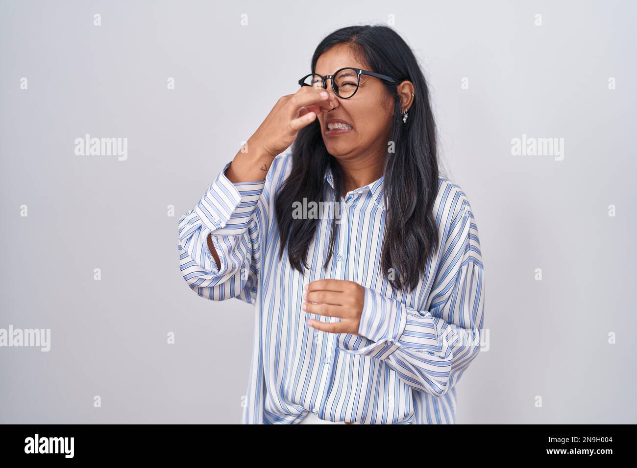 Young hispanic woman wearing glasses smelling something stinky and