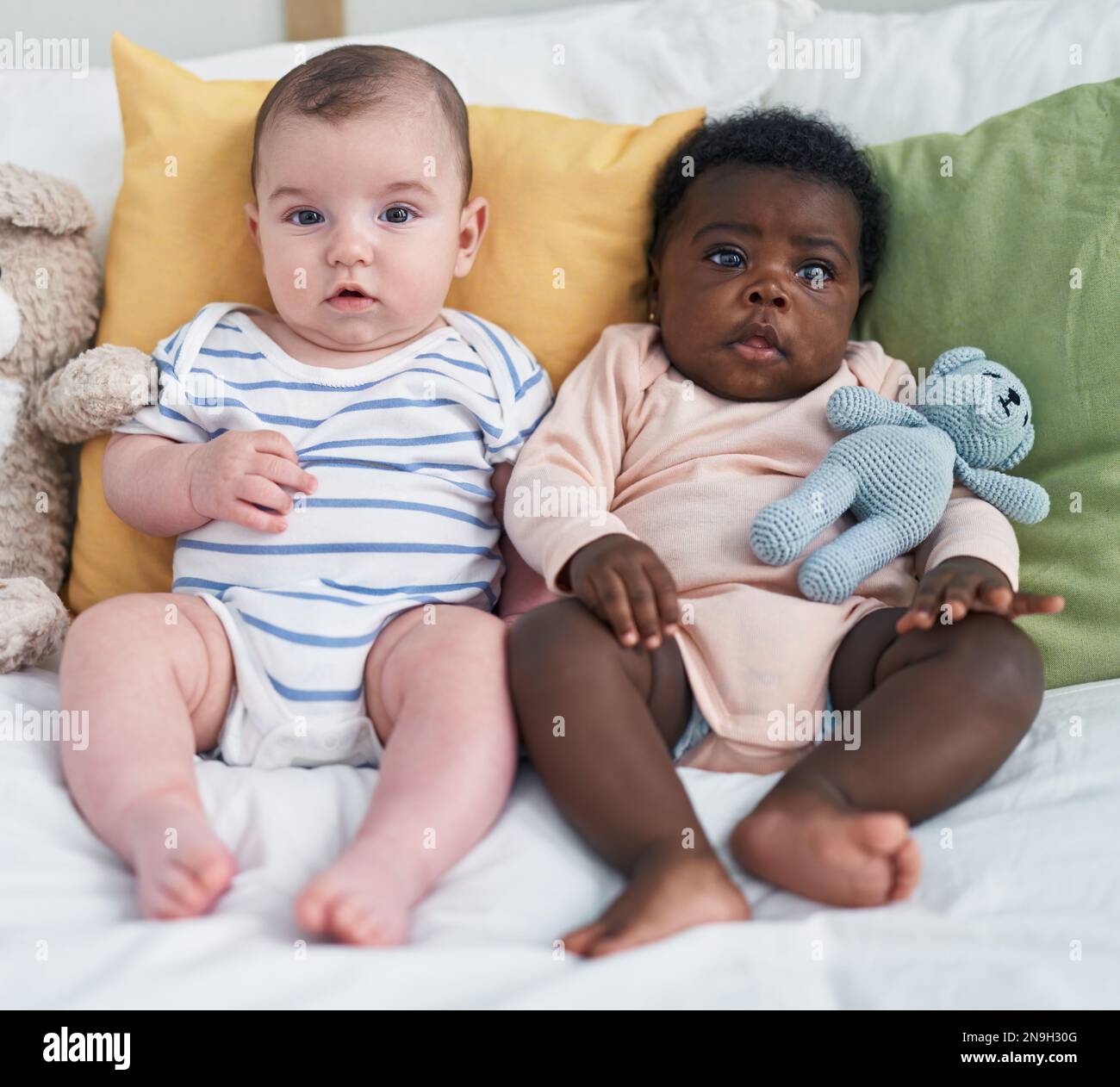 Two adorable babies sitting on bed at bedroom Stock Photo - Alamy