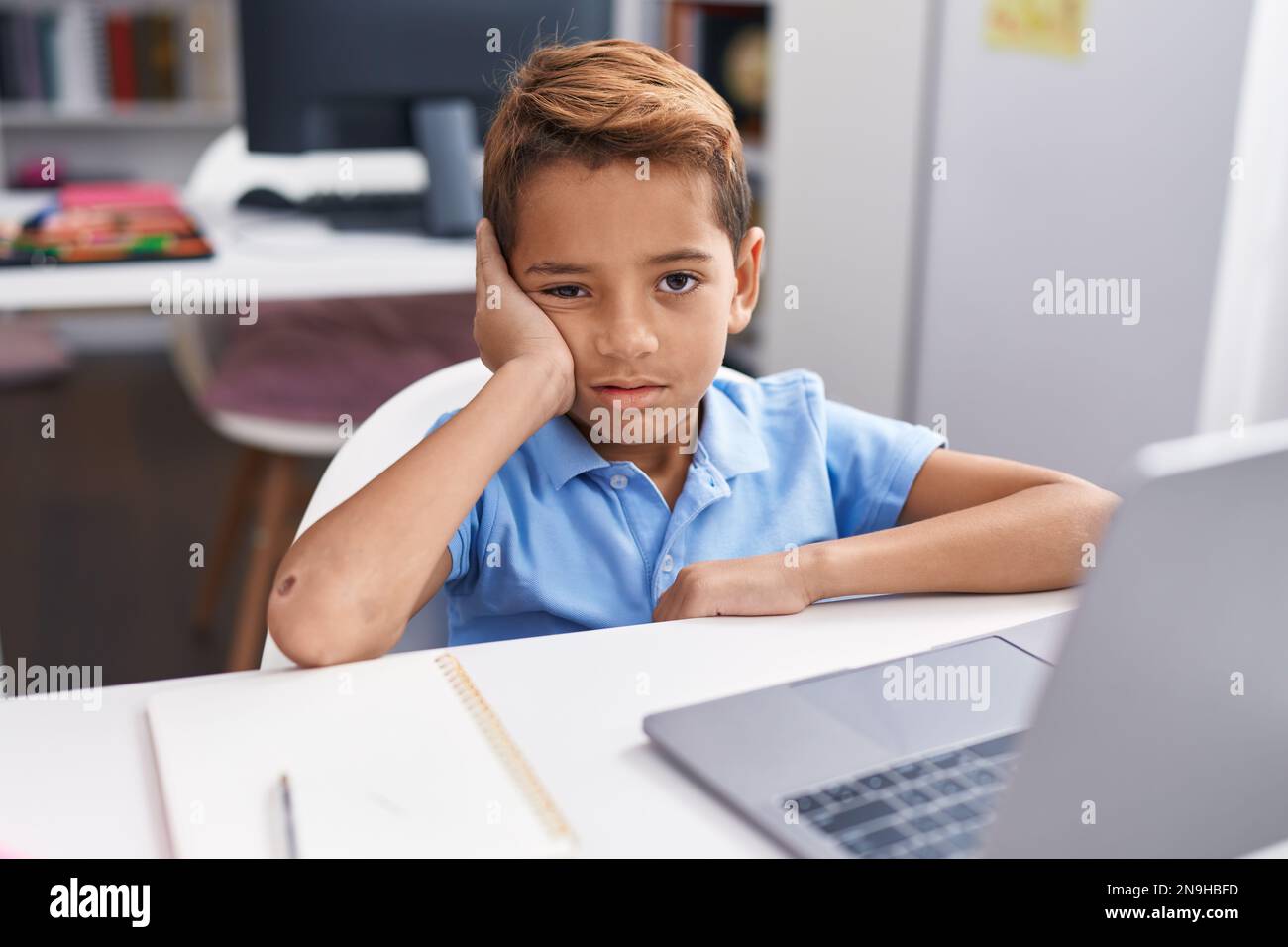Adorable hispanic boy student using computer with tired expression at ...