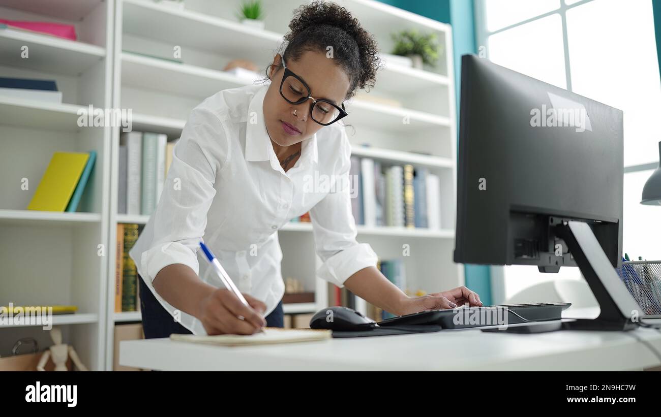 African american woman student using computer writing on notebook at ...