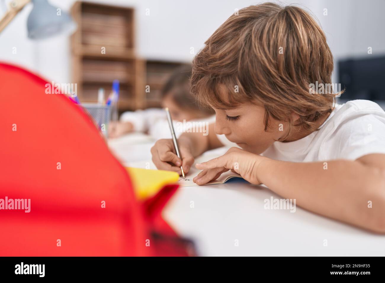 Brother and sister students writing on notebook studying at classroom ...