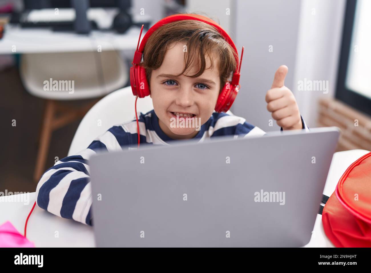Adorable hispanic boy student using laptop doing ok gesture with thumb ...