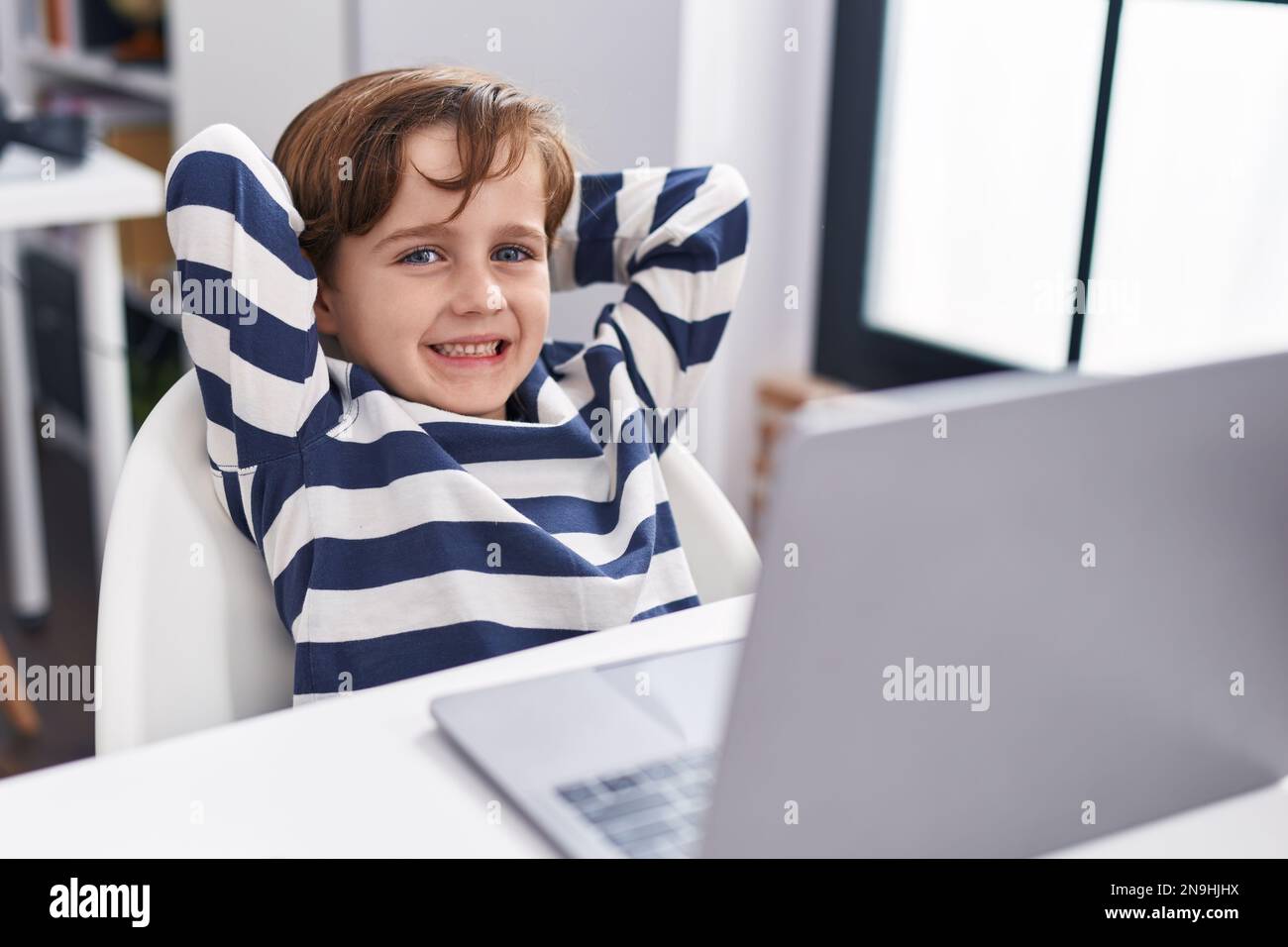 Adorable hispanic boy student using computer relaxed with hands on head ...