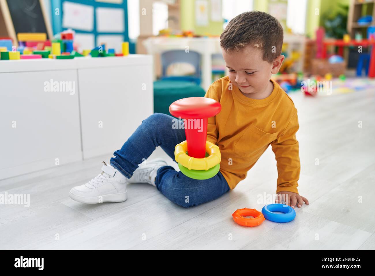 Adorable caucasian boy playing with hoops toy sitting on floor at ...