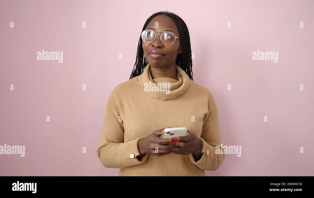 African woman smiling using smartphone over isolated pink background ...