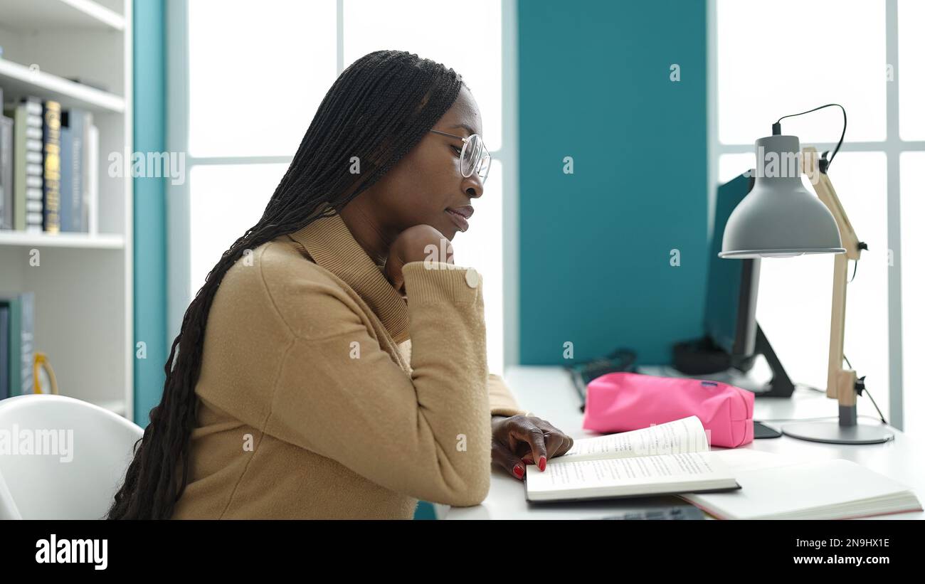 African woman reading a book sitting on desk at library university ...