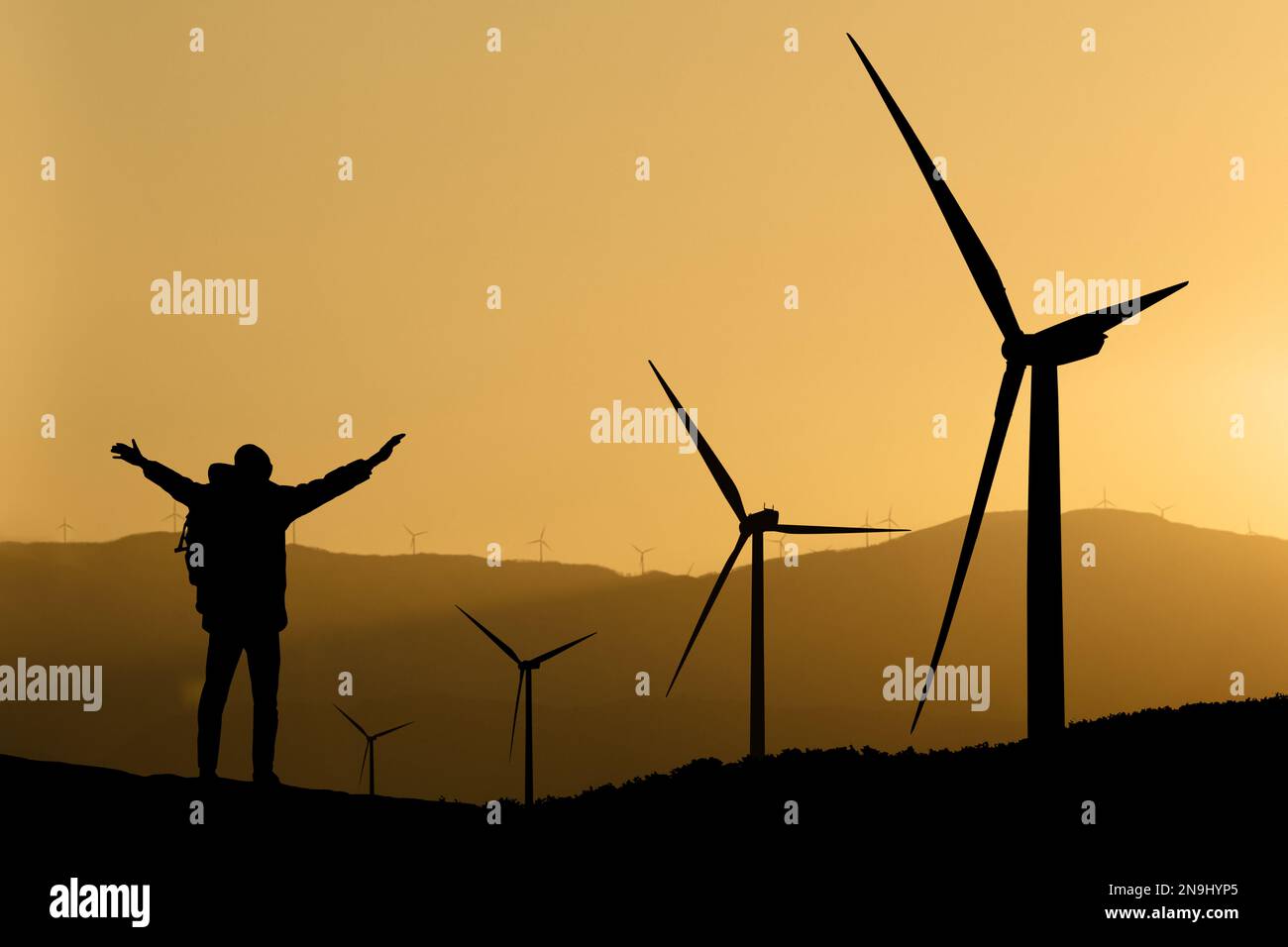 Silhouettes of a traveler with a backpack and wind turbines at sunset Stock Photo