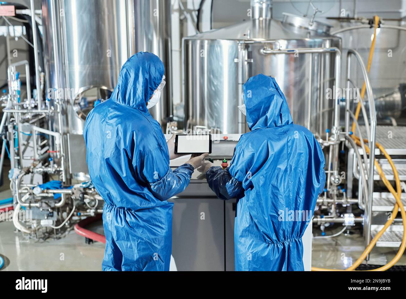 Back view of two workers using control panel while operating equipment at chemical factory Stock Photo