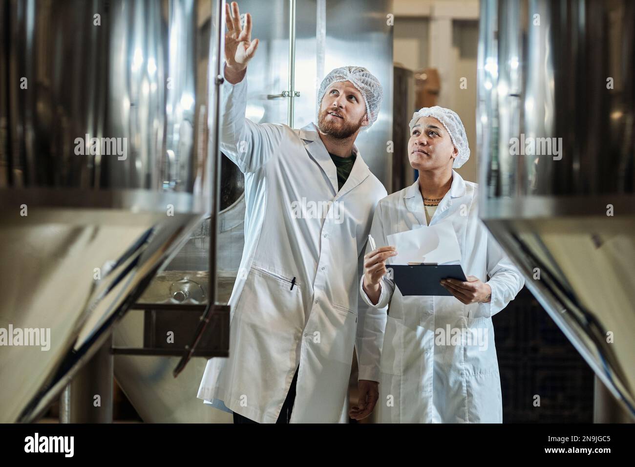Waist up portrait of two workers wearing lab coats inspecting equipment
