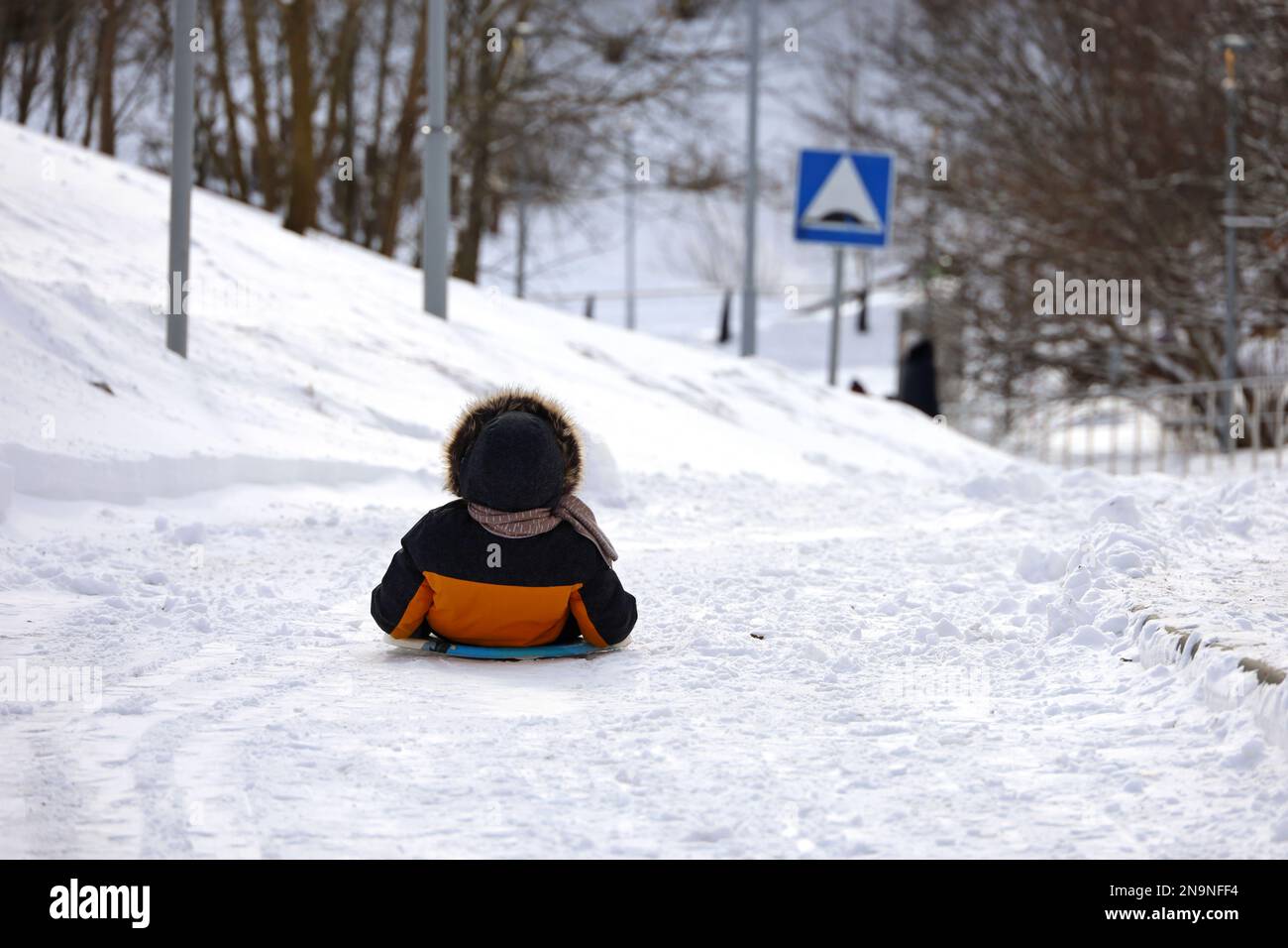 Child riding on sledge by the snowy road, little boy during tubing in winter park Stock Photo