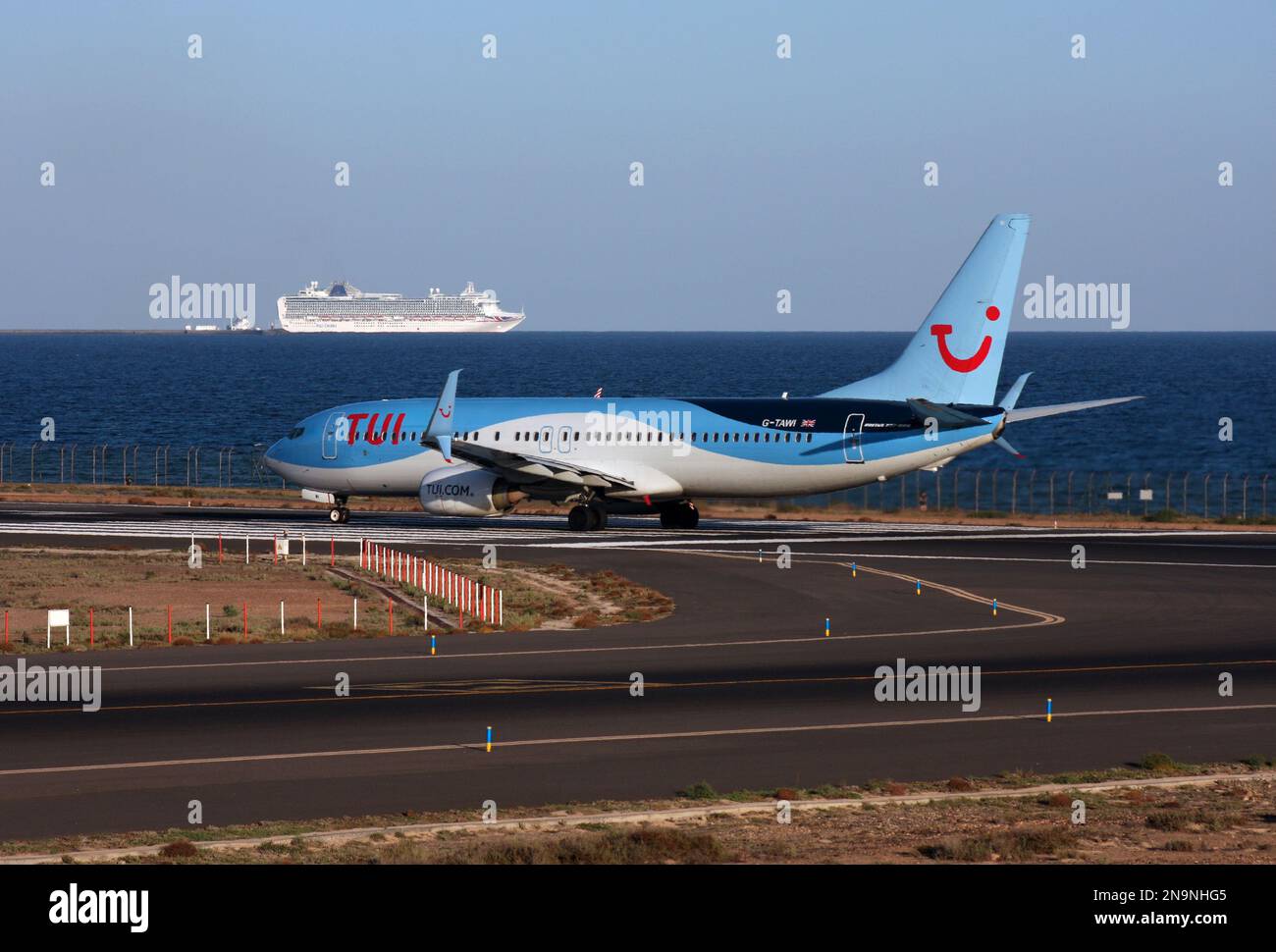 A Boeing 737-800 of TUI lines up to depart Lanzarote Arrecife Airport Canary Islands with a cruise ship to the rear Stock Photo
