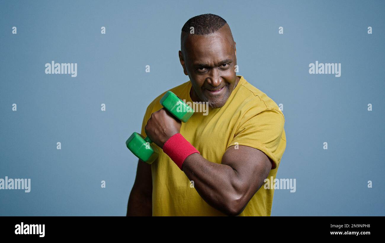 Mature strong athletic man coach pumping biceps with dumbbell in studio