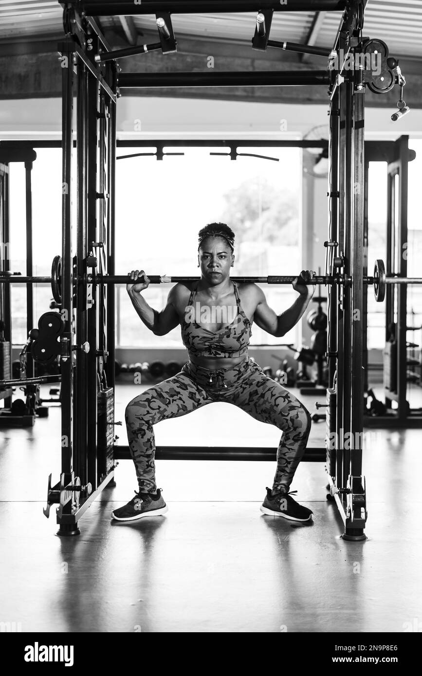 Determined woman doing squat exercises with a barbell and barbell at the gym. Body strengthening. Stock Photo