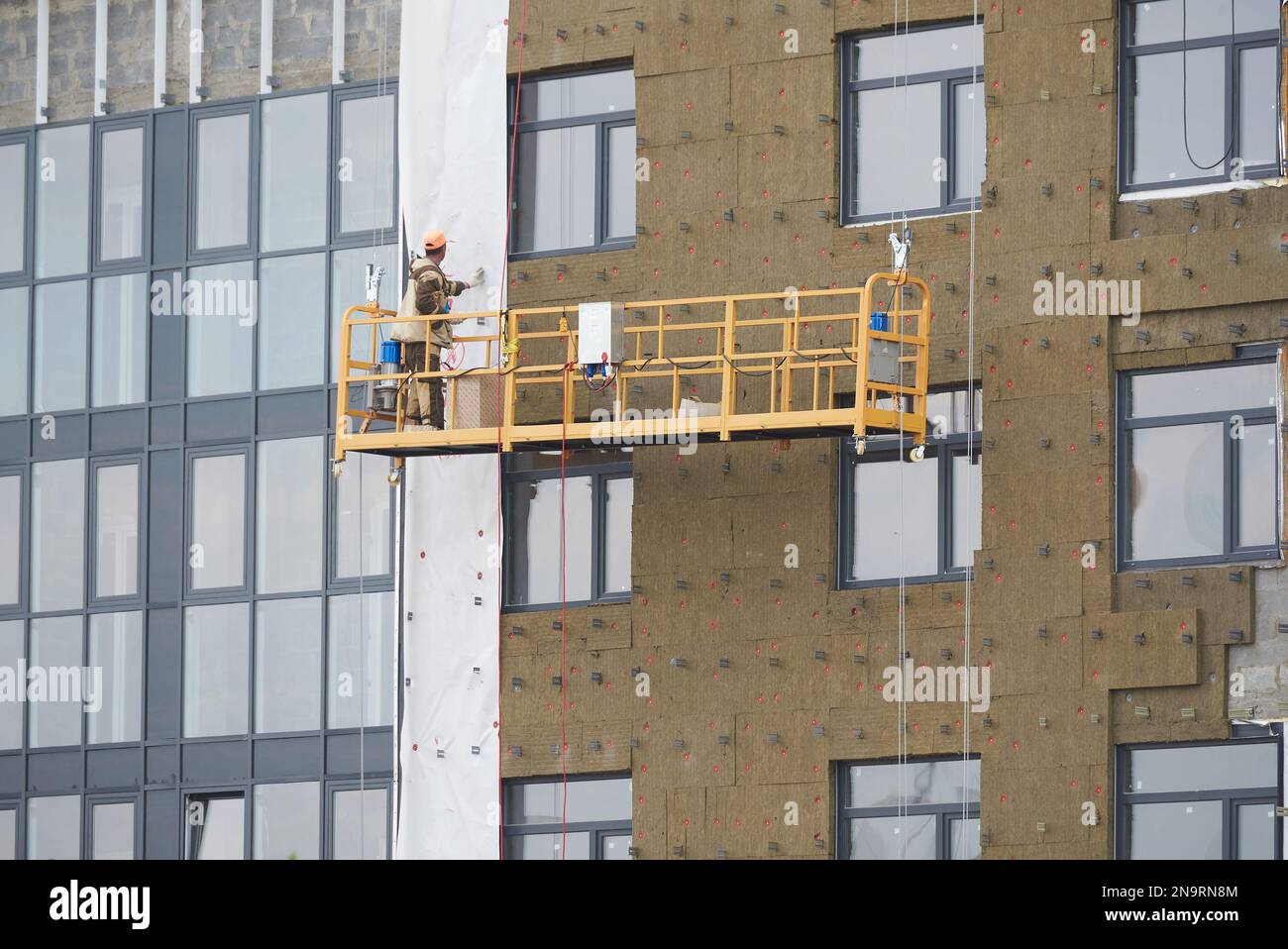 Builder works in a special suspended platform and insulate external wall of an apartment building. Stock Photo