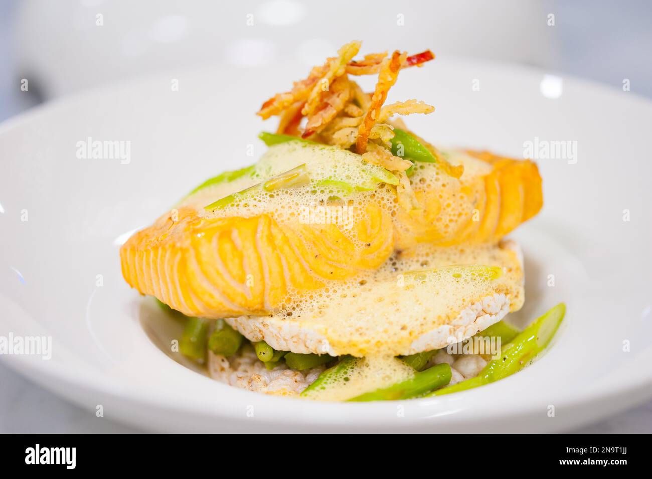 Close-up of salmon fillet with rice cakes, green beans, lemon butter garlic sauce. Seafood dish on white plate. Healthy lunch on cafe table. food, meal. Stock Photo