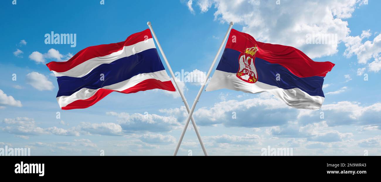 two crossed flags Serbia and Thailand waving in wind at cloudy sky ...