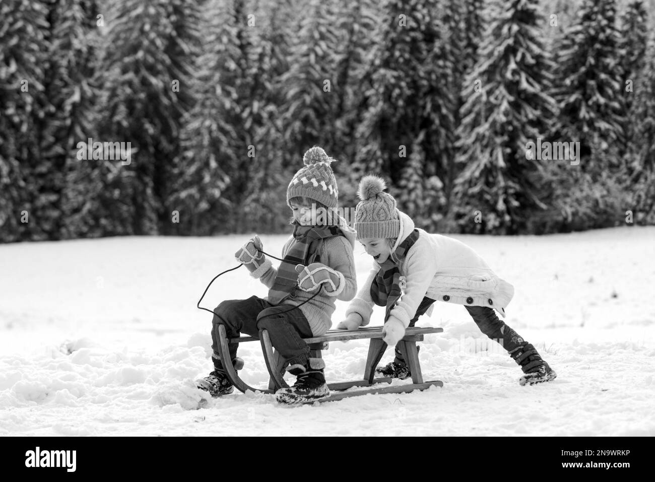 Funny children in snow ride on sled. Winter outdoors games. Happy Christmas family vacation concept. Kids enjoy the holiday. Stock Photo