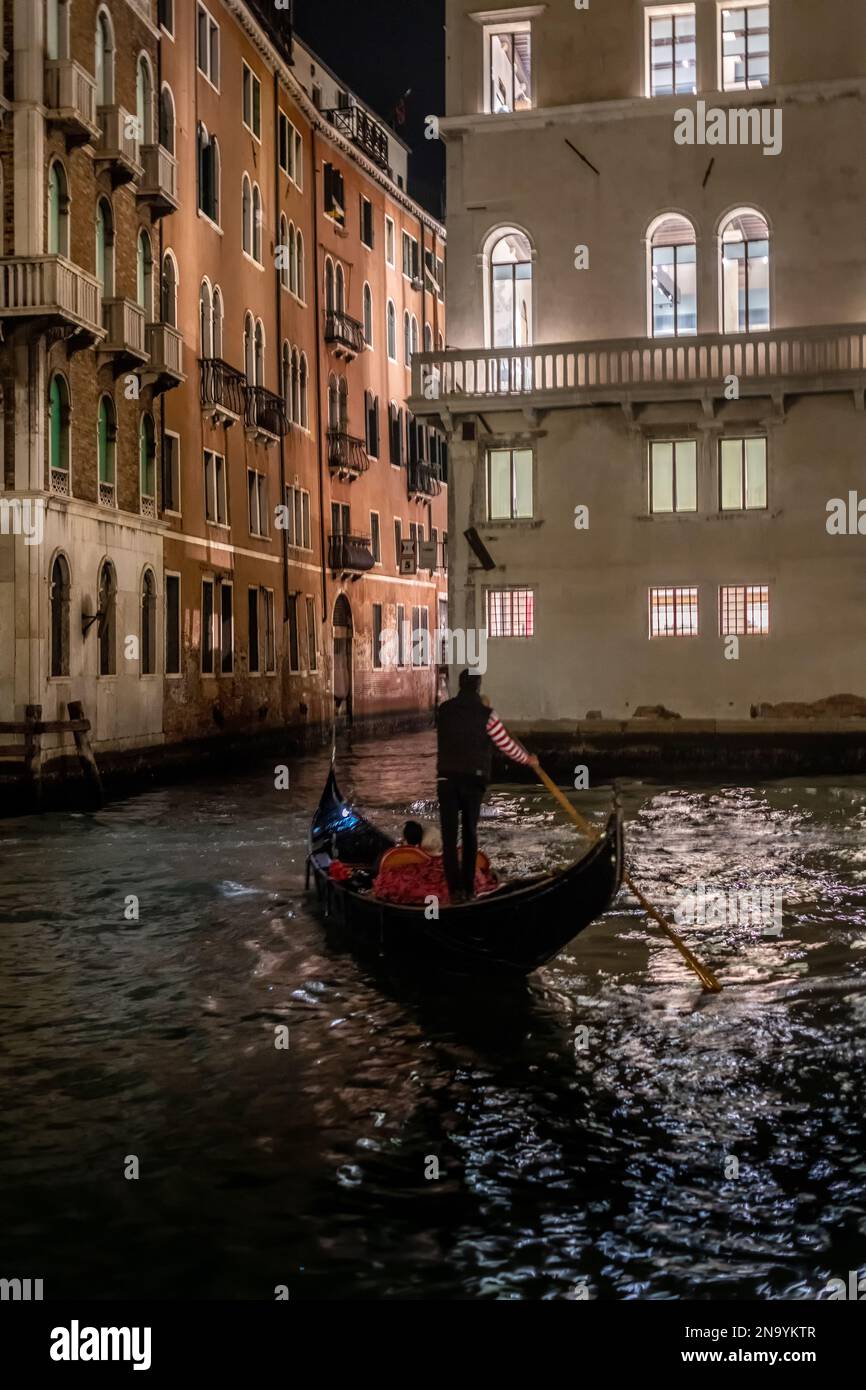 Gondolier steering a gondola, a traditional Venetian row boat on Grand Canal at night in Venice, Italy Stock Photo
