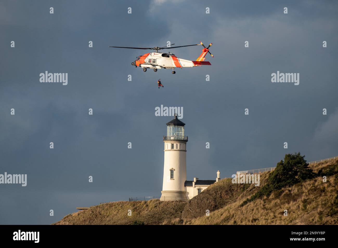 US Coast Guard Helicoptor flying near the Cape Disappointment North Head Lighthouse during a training mission Stock Photo