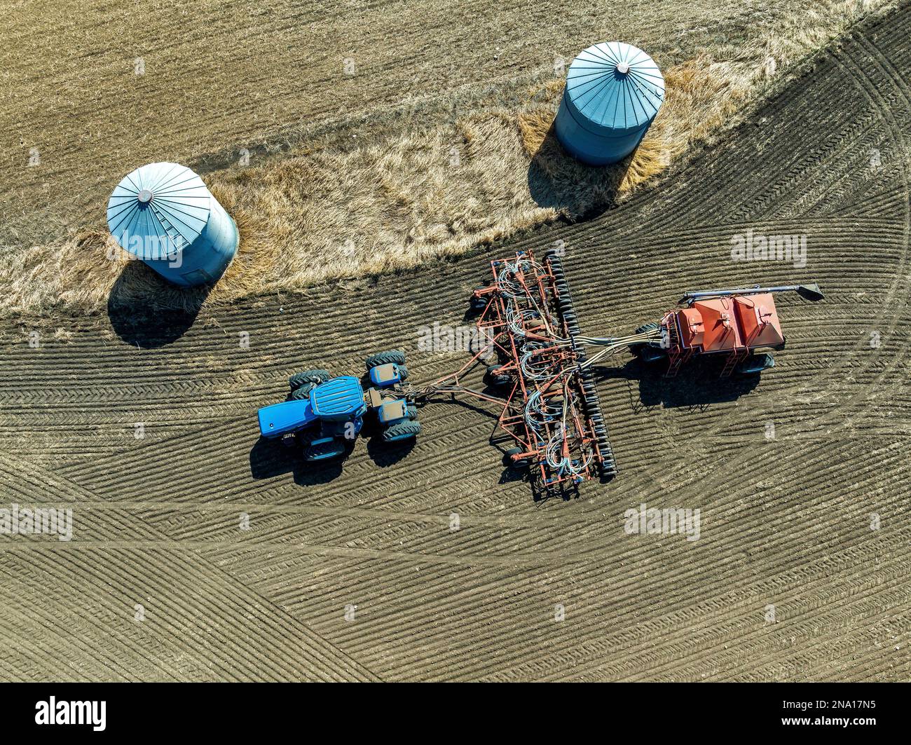 Aerial overhead view of tractor and seeder, seeding field beside metal