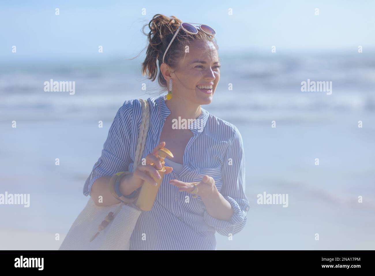 happy elegant 40 years old woman with sunscreen and white straw bag at