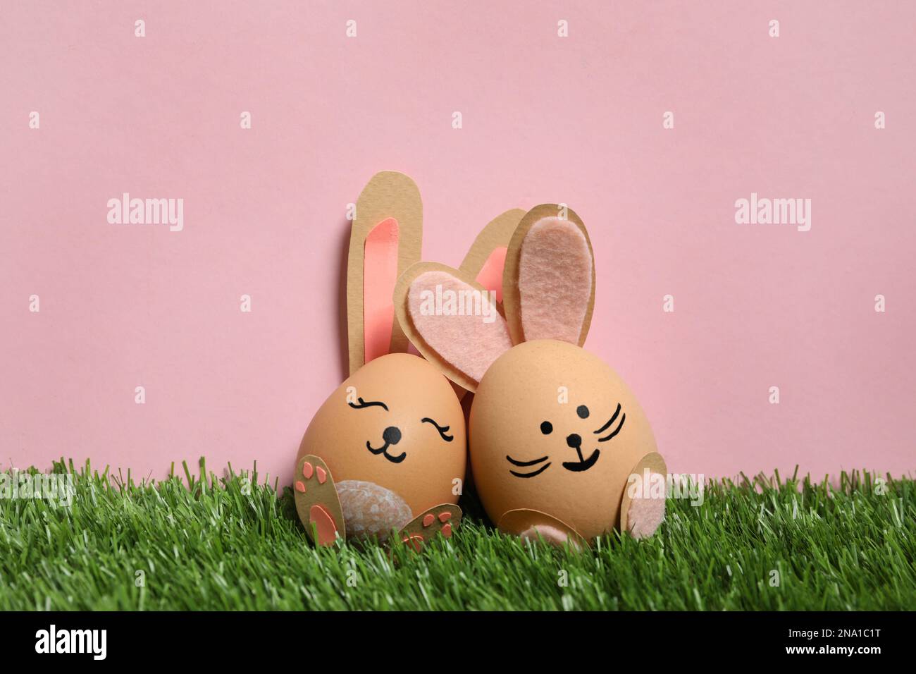 Easter eggs as cute bunnies on green grass against pink background ...