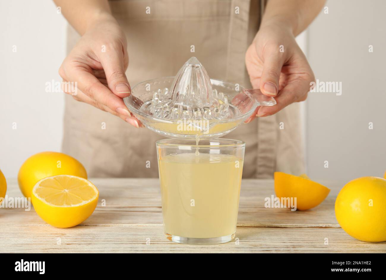 Woman pouring freshly squeezed lemon juice in glass at white wooden table, closeup Stock Photo