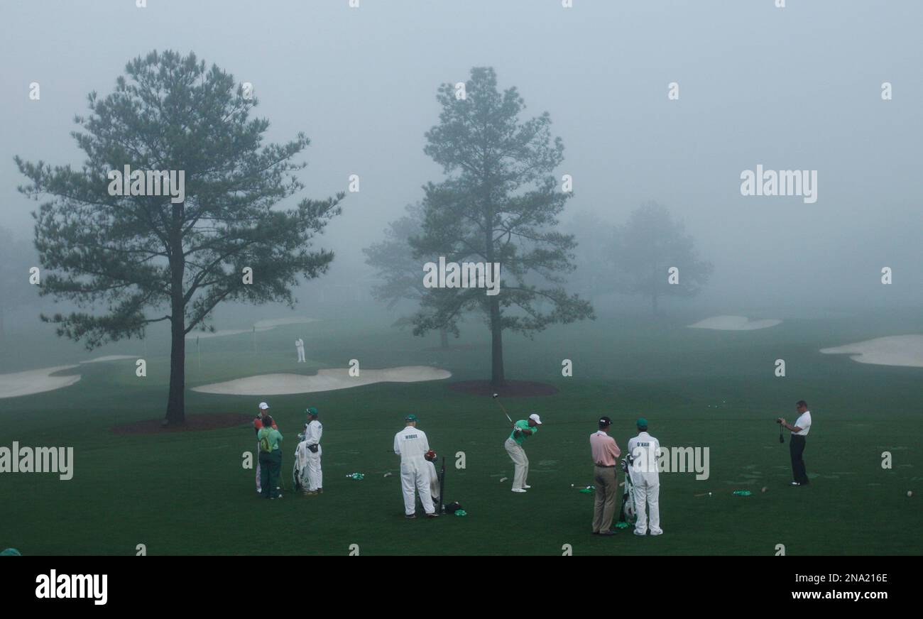 Surrounded by caddies and coaches, Tiger Woods, center, hits on the fog