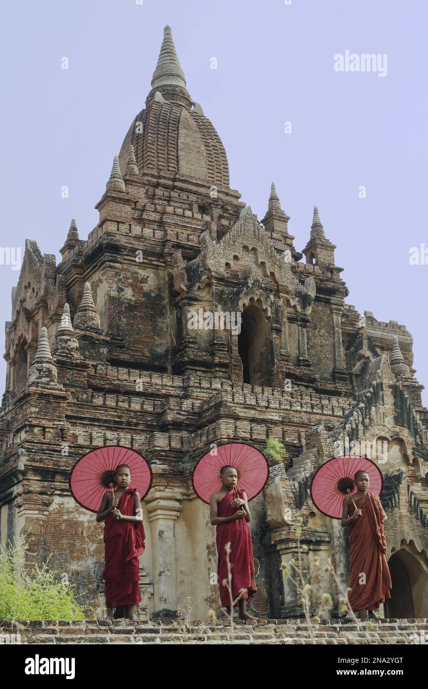 Monks with umbrellas stand in front of the ruins of a Buddhist temple; Bagan, Myanmar Stock Photo