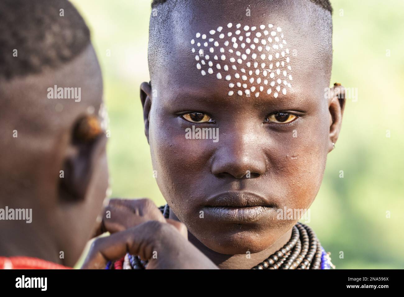 Young Karo man getting his face decorated with traditional face paint at Kortcho Village; Omo Valley, Ethiopia Stock Photo